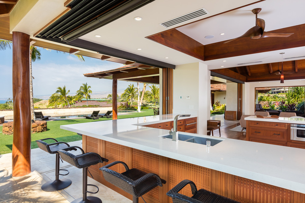 Inspiration for a large tropical l-shaped open plan kitchen in Hawaii with a double-bowl sink, recessed-panel cabinets, medium wood cabinets, quartz benchtops, stainless steel appliances, limestone floors and a peninsula.