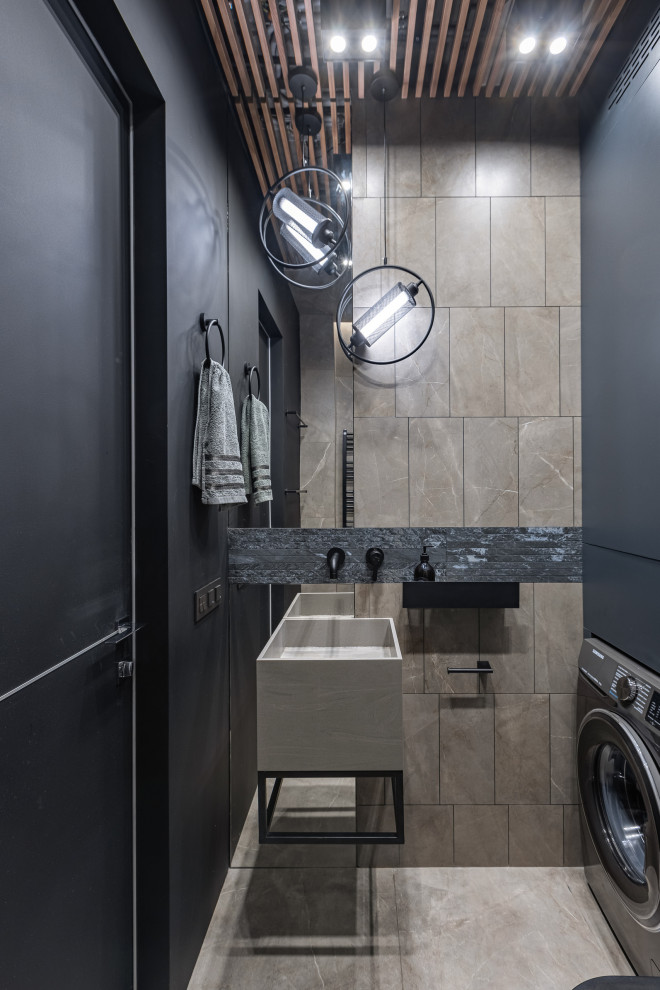 Пример оригинального дизайна: ванная комната со стиральной машиной в стиле лофт с бежевой плиткой, черными стенами, подвесной раковиной, бежевым полом, тумбой под одну раковину и деревянным потолком