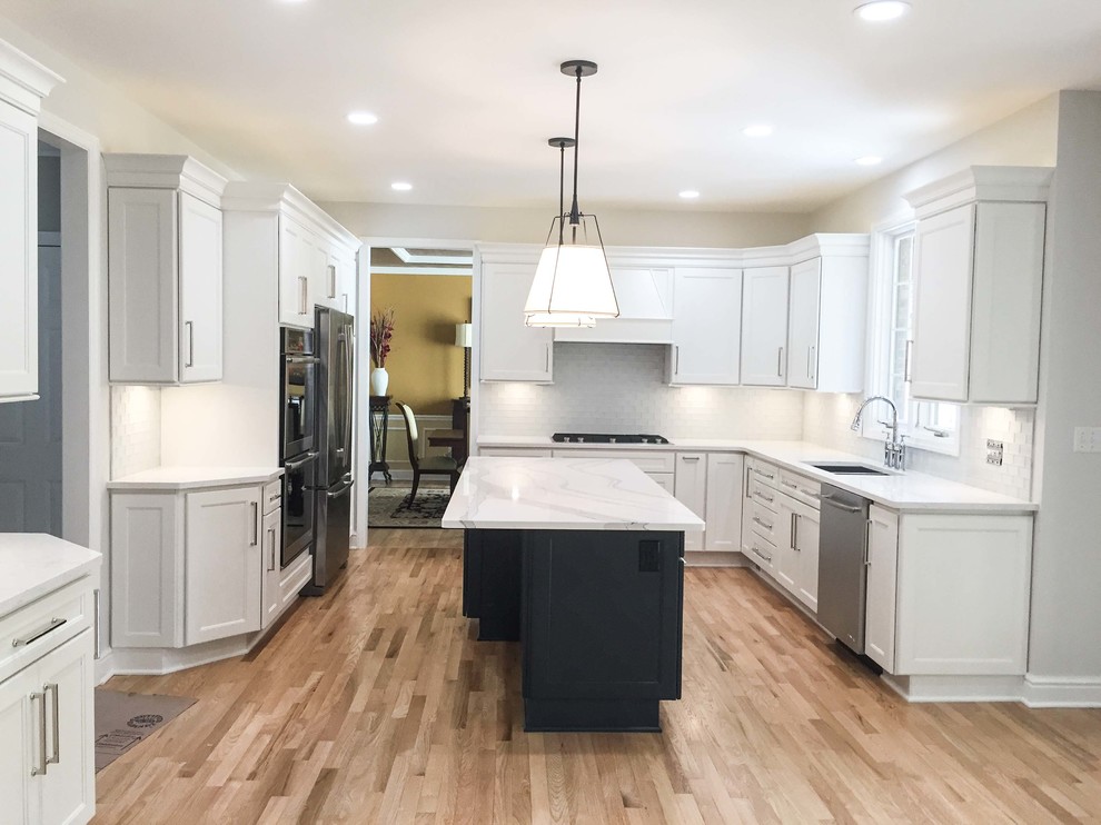 Kitchen - large transitional u-shaped light wood floor kitchen idea with an undermount sink, shaker cabinets, white cabinets, quartz countertops, white backsplash, glass tile backsplash, stainless steel appliances and an island