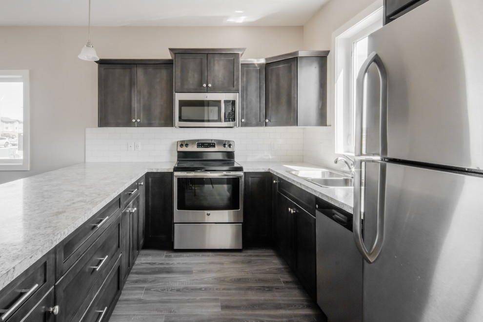 Example of a mid-sized transitional u-shaped medium tone wood floor open concept kitchen design in Calgary with a drop-in sink, shaker cabinets, dark wood cabinets, laminate countertops, white backsplash, subway tile backsplash, stainless steel appliances and a peninsula