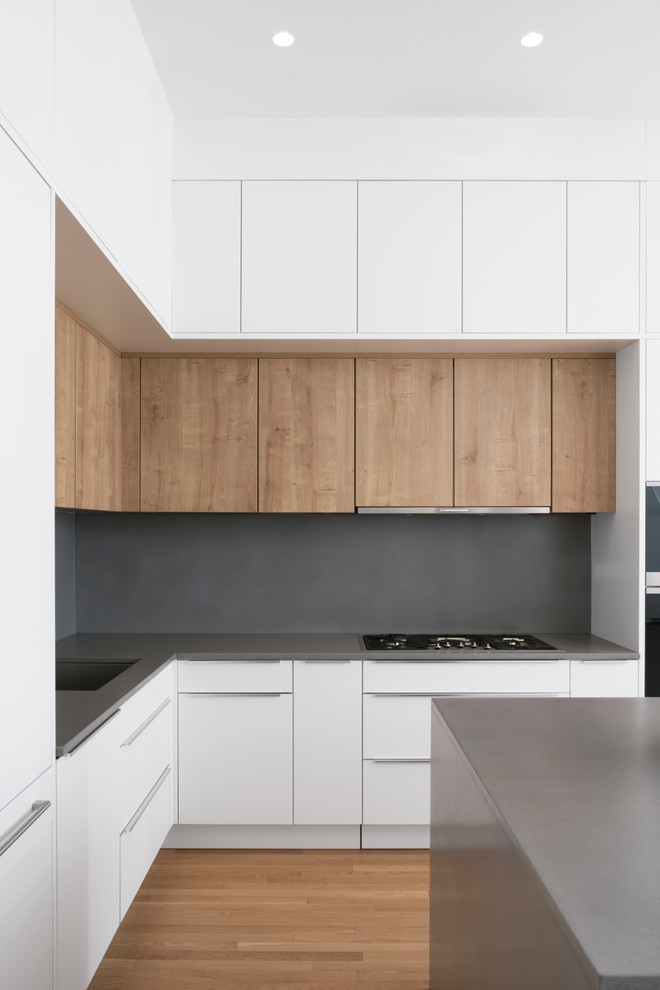 This is an example of a mid-sized contemporary l-shaped open plan kitchen in New York with a single-bowl sink, flat-panel cabinets, white cabinets, concrete benchtops, grey splashback, cement tile splashback, stainless steel appliances, light hardwood floors, with island, brown floor and grey benchtop.