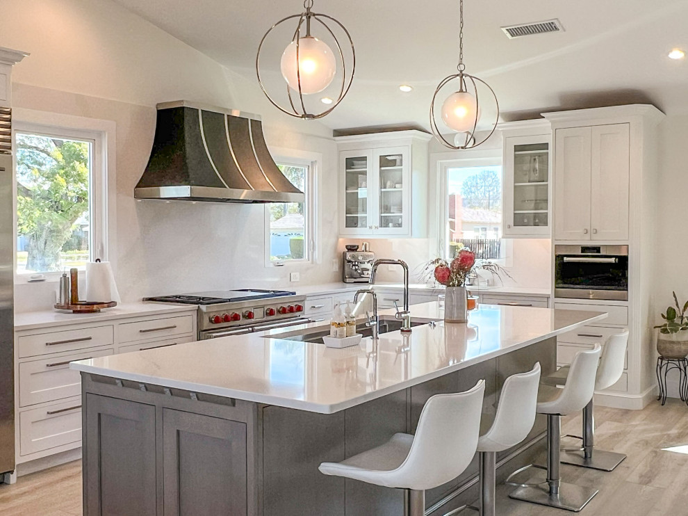 Example of a transitional kitchen design with shaker cabinets, white cabinets, white backsplash, stainless steel appliances, an island and white countertops