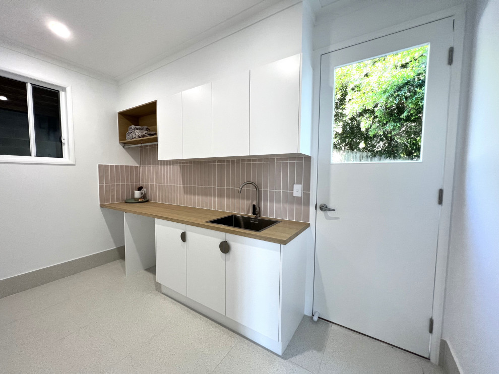 Design ideas for a mid-sized contemporary galley dedicated laundry room in Sunshine Coast with a drop-in sink, flat-panel cabinets, white cabinets, laminate benchtops, pink splashback, ceramic splashback, ceramic floors, a side-by-side washer and dryer, multi-coloured floor and brown benchtop.