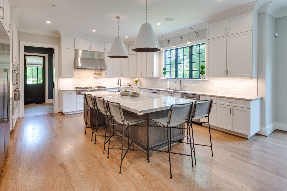 Inspiration for a large transitional u-shaped medium tone wood floor open concept kitchen remodel in DC Metro with an undermount sink, recessed-panel cabinets, white cabinets, marble countertops, white backsplash, marble backsplash, stainless steel appliances and an island