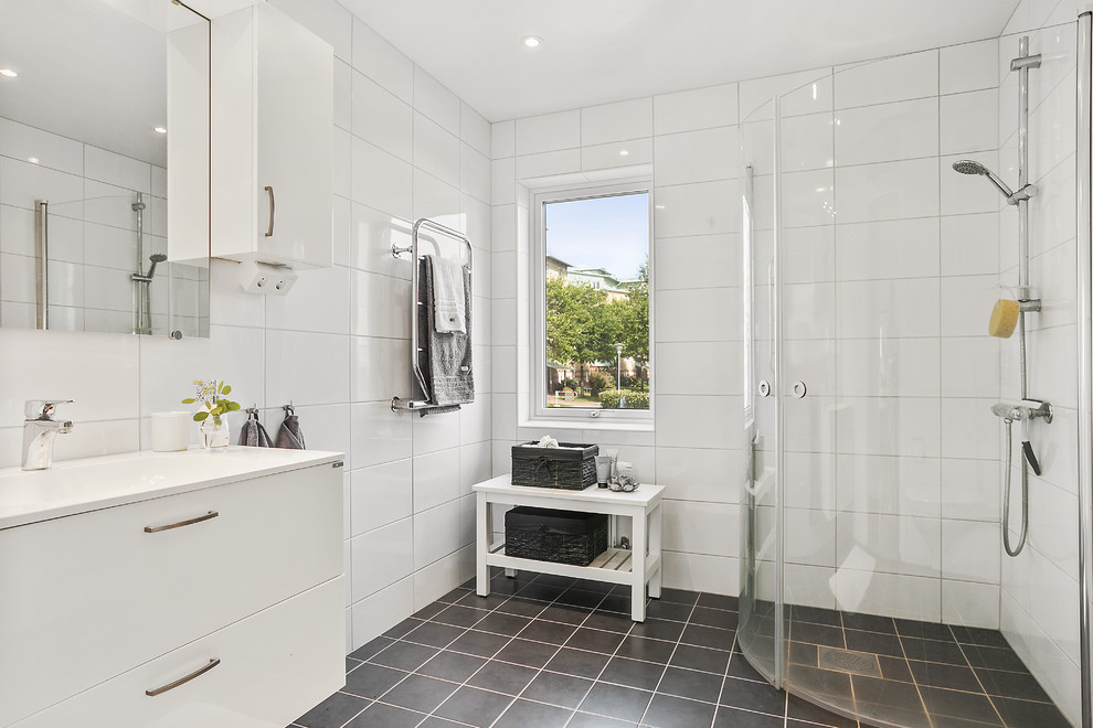 Scandinavian 3/4 bathroom in Gothenburg with flat-panel cabinets, white cabinets, a corner shower, white tile, a console sink, black floor and a hinged shower door.
