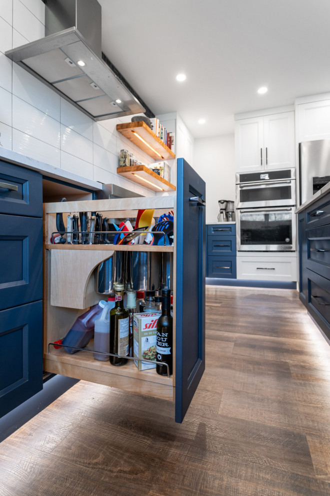 Example of a large transitional u-shaped dark wood floor and brown floor eat-in kitchen design with an undermount sink, recessed-panel cabinets, blue cabinets, quartz countertops, white backsplash, ceramic backsplash, stainless steel appliances, an island and white countertops