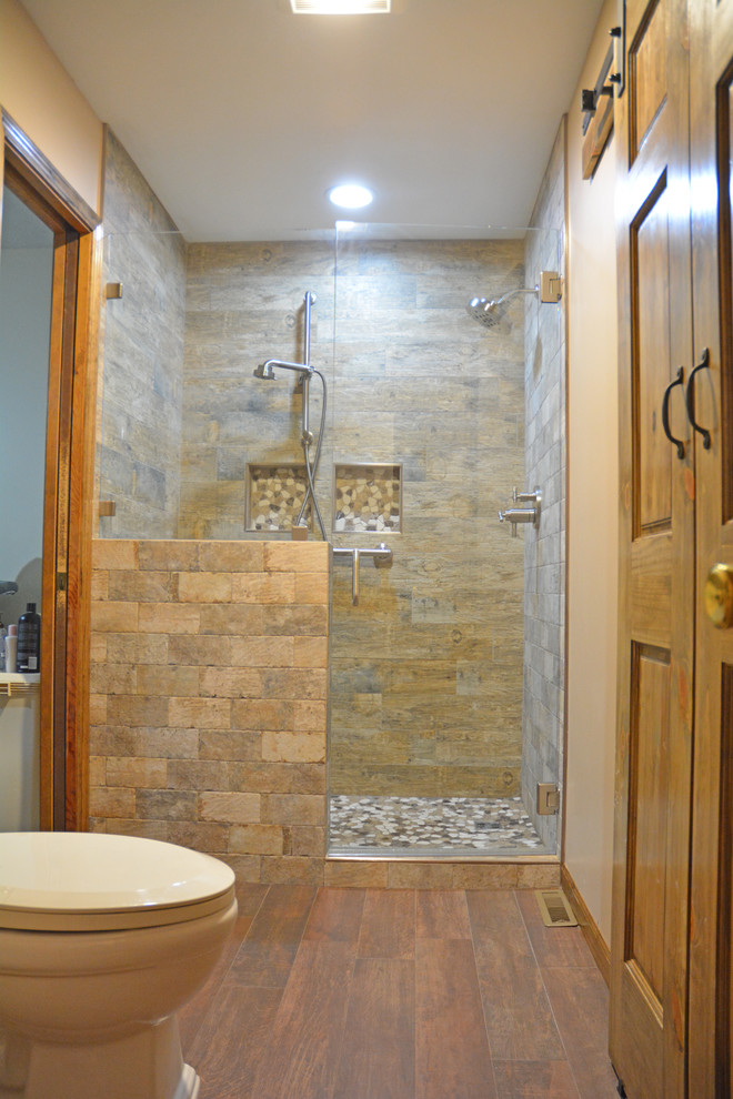 Inspiration for a mid-sized rustic master brown tile and ceramic tile ceramic tile and brown floor alcove shower remodel with raised-panel cabinets, light wood cabinets, a two-piece toilet, beige walls, an integrated sink, marble countertops, a hinged shower door and gray countertops
