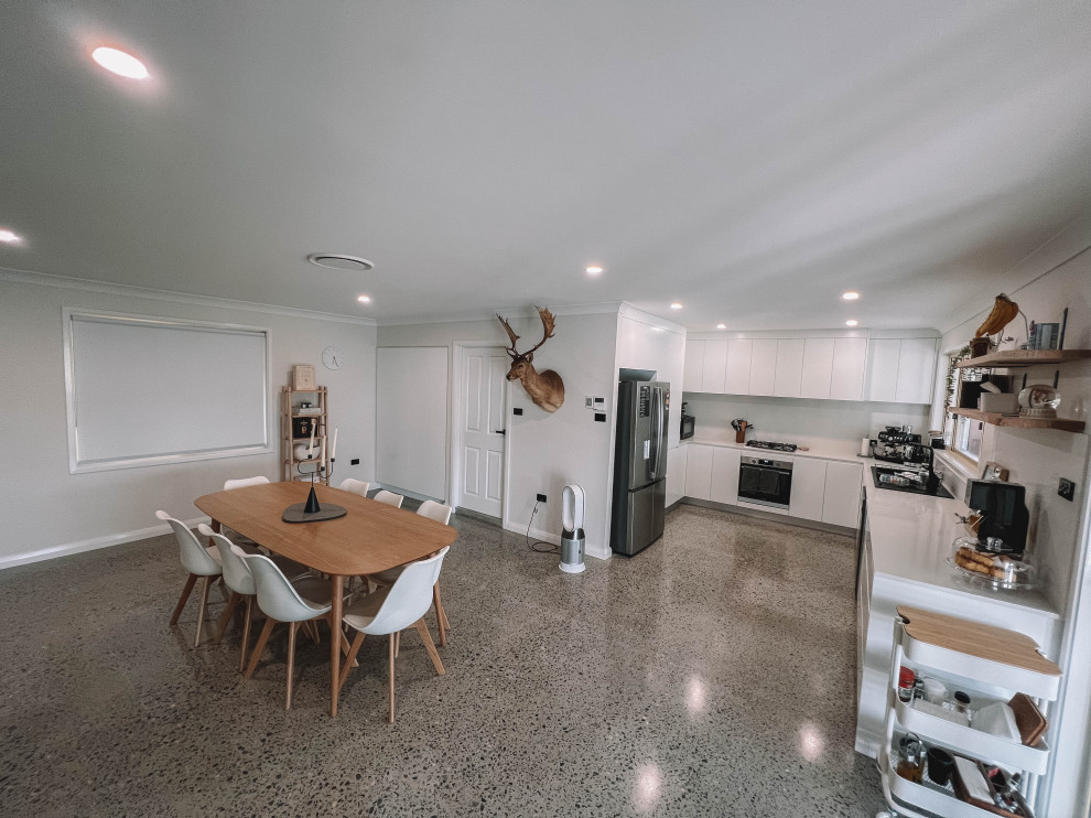 Small scandi u-shaped open plan kitchen in Sydney with a double-bowl sink, flat-panel cabinets, white cabinets, engineered stone countertops, white splashback, engineered quartz splashback, black appliances, concrete flooring, no island, grey floors, white worktops and a timber clad ceiling.