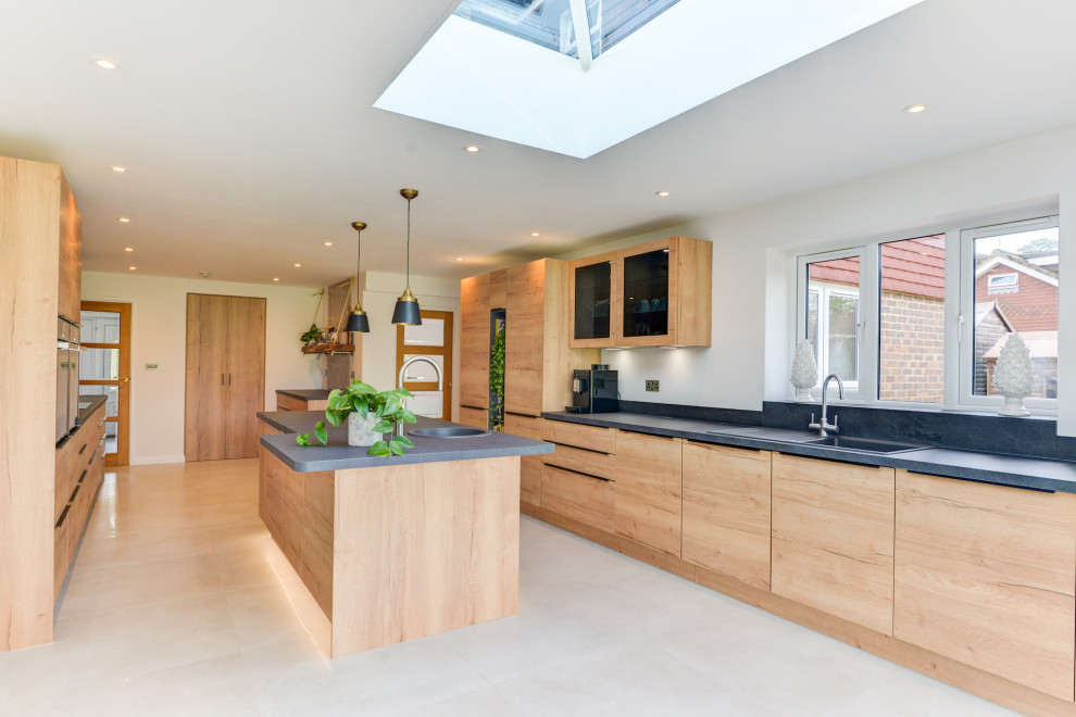 Large contemporary galley open plan kitchen in Sussex with an integrated sink, flat-panel cabinets, medium wood cabinets, laminate benchtops, grey splashback, panelled appliances, porcelain floors, with island, white floor and grey benchtop.