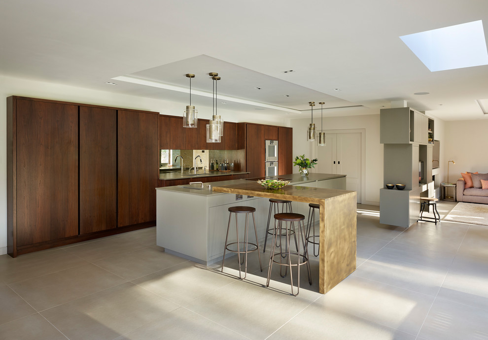 Photo of an expansive contemporary l-shaped open plan kitchen in Kent with a double-bowl sink, flat-panel cabinets, dark wood cabinets, quartzite benchtops, metallic splashback, mirror splashback, stainless steel appliances, porcelain floors, with island and beige floor.