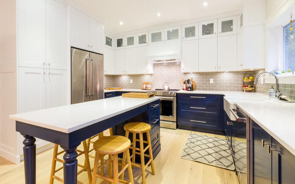 Inspiration for a large transitional u-shaped light wood floor and beige floor open concept kitchen remodel with a farmhouse sink, shaker cabinets, blue cabinets, quartz countertops, gray backsplash, glass tile backsplash, stainless steel appliances, an island and white countertops