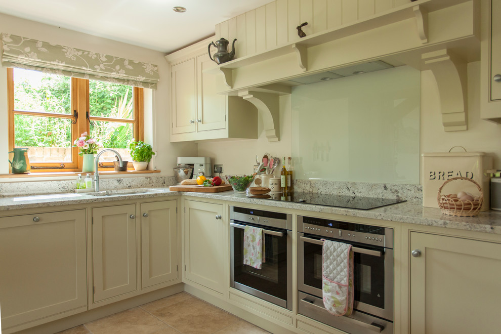 Large traditional l-shaped eat-in kitchen in Gloucestershire with a drop-in sink, shaker cabinets, green cabinets, granite benchtops, white splashback, glass sheet splashback, stainless steel appliances, travertine floors, with island, beige floor and green benchtop.