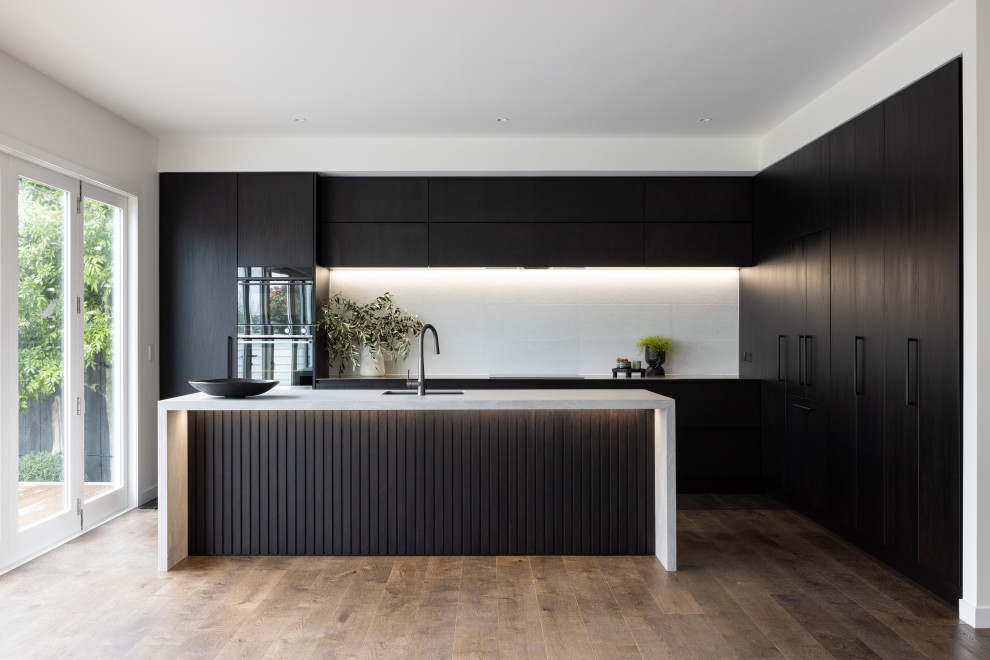 Inspiration for a contemporary eat-in kitchen in Auckland with an integrated sink, dark wood cabinets, white splashback, ceramic splashback, stainless steel appliances, dark hardwood floors, with island, brown floor and grey benchtop.