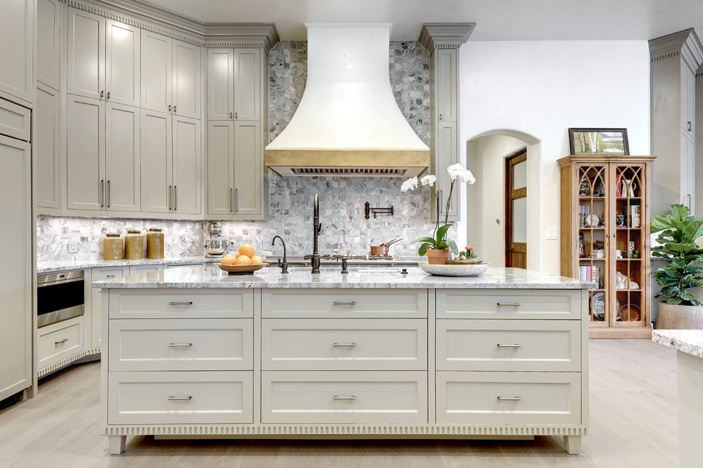 Example of a transitional l-shaped light wood floor and gray floor kitchen design in Austin with shaker cabinets, gray cabinets, gray backsplash, paneled appliances and an island