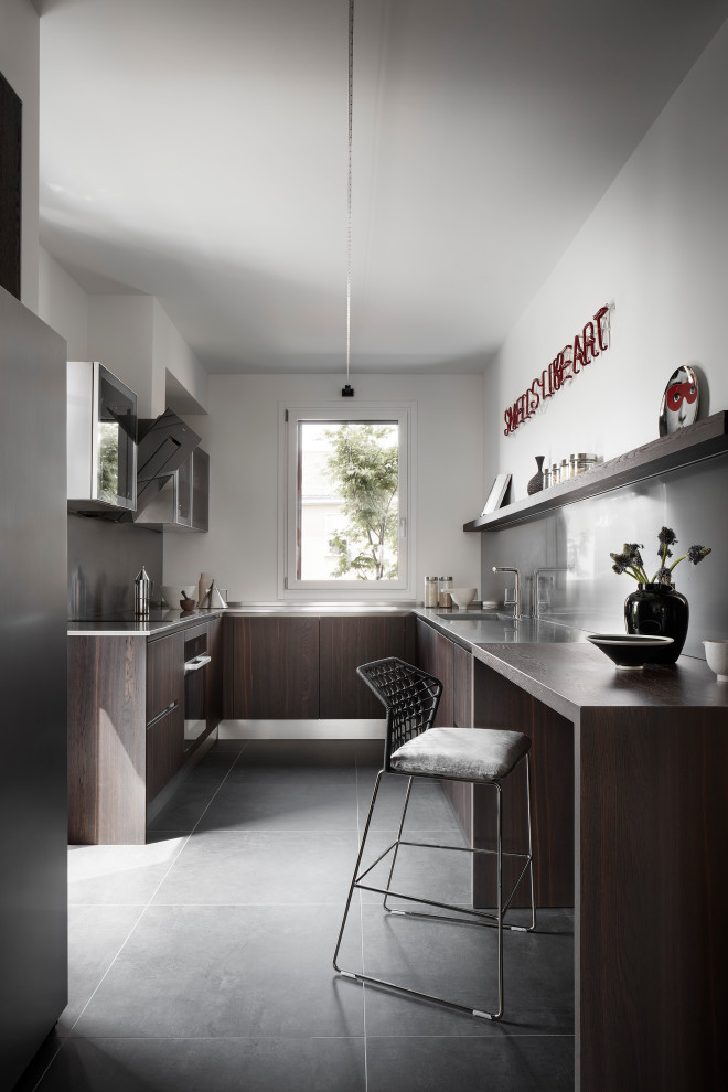 Inspiration for a medium sized modern u-shaped open plan kitchen in Bologna with a single-bowl sink, beaded cabinets, dark wood cabinets, stainless steel worktops, grey splashback, black appliances, porcelain flooring, no island, black floors and grey worktops.