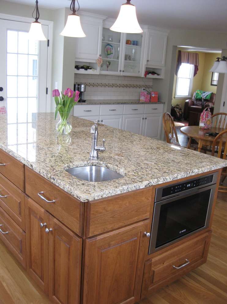 Inspiration for a transitional u-shaped medium tone wood floor eat-in kitchen remodel in Boston with an undermount sink, raised-panel cabinets, white cabinets, granite countertops, white backsplash, ceramic backsplash, stainless steel appliances, an island and beige countertops