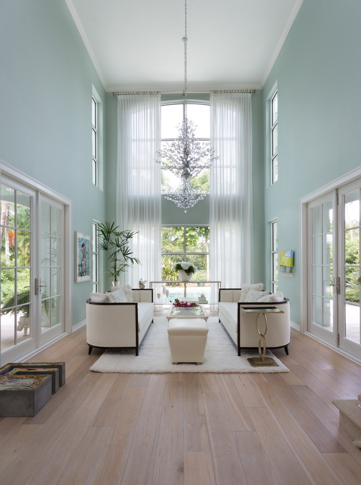 This is an example of an expansive tropical formal open concept living room in Miami with blue walls, light hardwood floors and no tv.