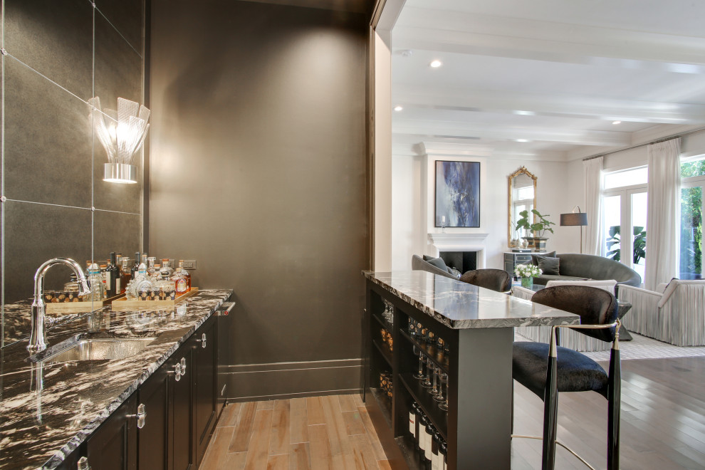 Design ideas for a mid-sized transitional galley wet bar in New Orleans with an undermount sink, shaker cabinets, black cabinets, marble benchtops, mirror splashback, light hardwood floors, brown floor and black benchtop.