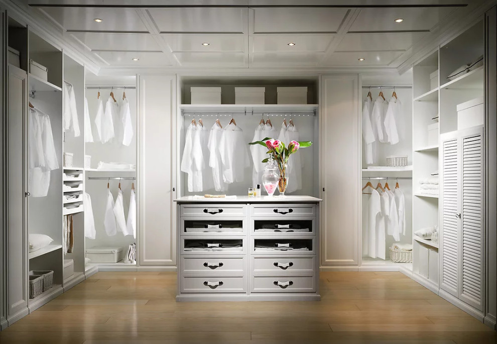 This is an example of a mid-sized gender-neutral walk-in wardrobe in New York with louvered cabinets, white cabinets, light hardwood floors, brown floor and wood.