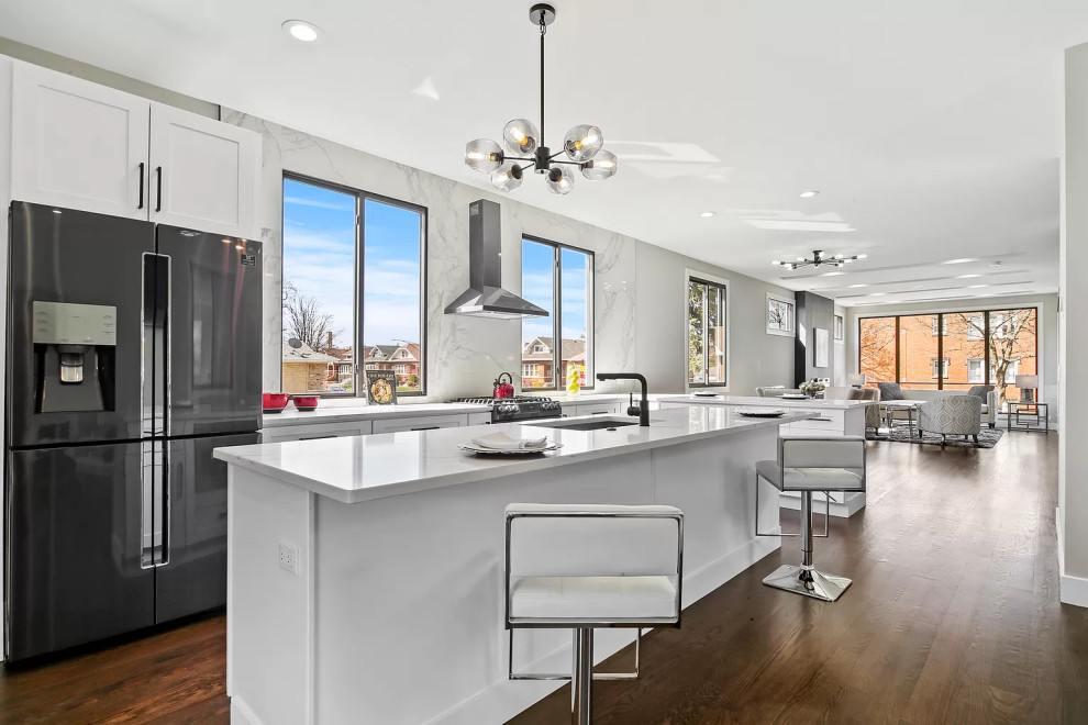 This is an example of a large contemporary l-shaped open plan kitchen in Chicago with a submerged sink, shaker cabinets, white cabinets, engineered stone countertops, white splashback, engineered quartz splashback, stainless steel appliances, dark hardwood flooring, an island, brown floors, white worktops and a drop ceiling.
