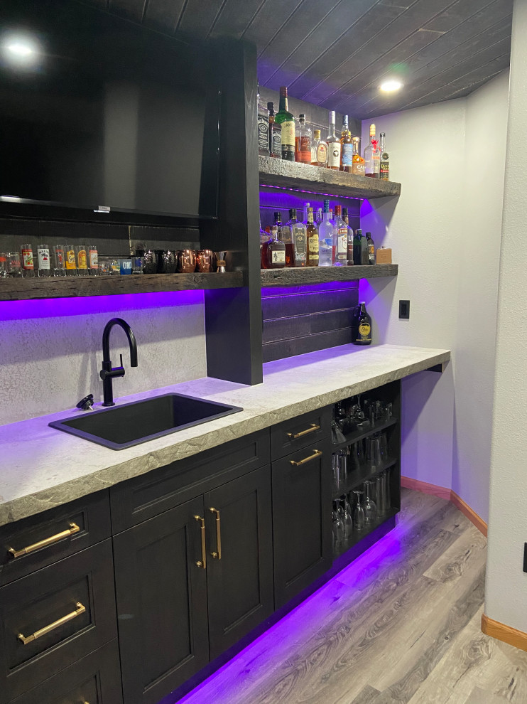 Photo of a mid-sized transitional l-shaped wet bar in Other with a drop-in sink, recessed-panel cabinets, dark wood cabinets, concrete benchtops, grey splashback, laminate floors, grey floor and grey benchtop.