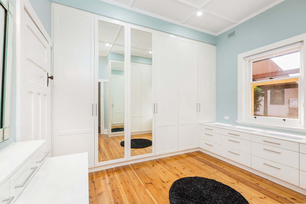 Design ideas for a mid-sized contemporary gender-neutral dressing room in Adelaide with shaker cabinets, white cabinets, light hardwood floors and brown floor.