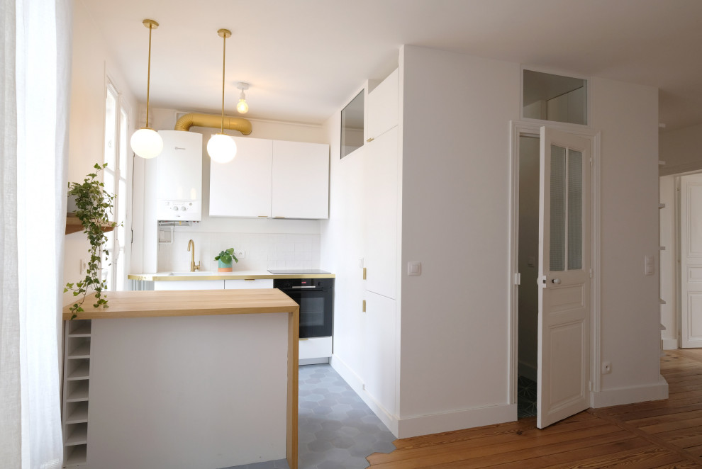 Photo of a small midcentury galley open plan kitchen in Paris with a submerged sink, flat-panel cabinets, white cabinets, laminate countertops, white splashback, ceramic splashback, integrated appliances, cement flooring, an island, blue floors and white worktops.