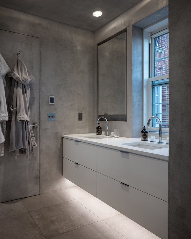 This is an example of a contemporary bathroom in New York with flat-panel cabinets, white cabinets, gray tile, grey walls, an undermount sink, grey floor and white benchtops.