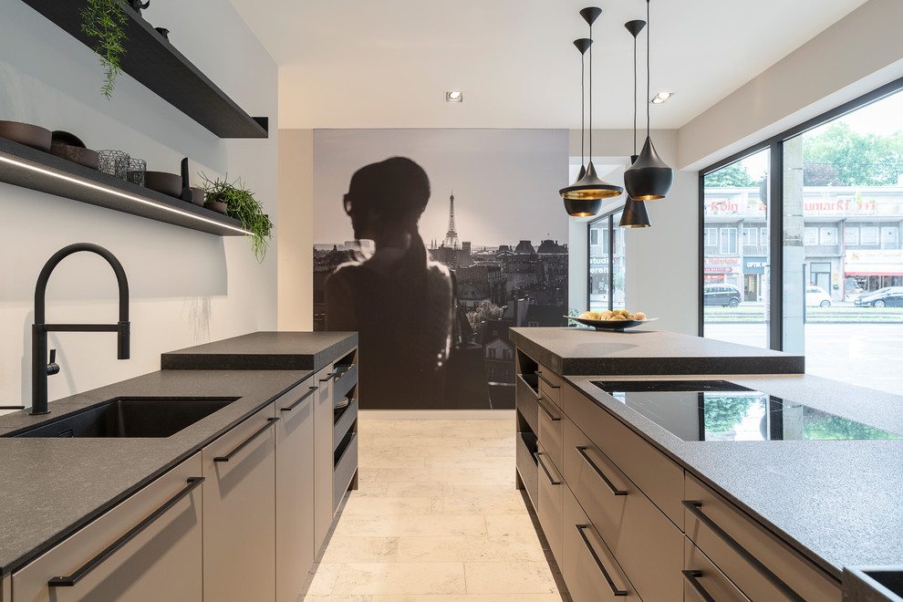Inspiration for a mid-sized contemporary galley open plan kitchen in Cologne with flat-panel cabinets, grey cabinets, solid surface benchtops, black appliances, marble floors, with island, beige floor, black benchtop, an undermount sink and white splashback.
