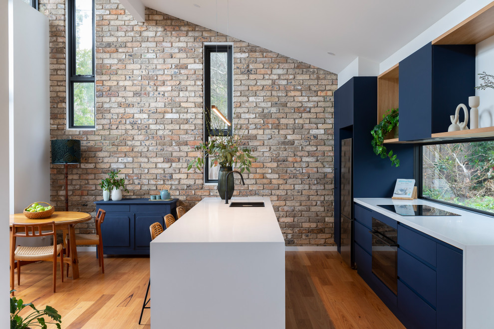 Design ideas for a mid-sized contemporary galley open plan kitchen in Canberra - Queanbeyan with an undermount sink, blue cabinets, quartz benchtops, window splashback, black appliances, medium hardwood floors, with island and white benchtop.