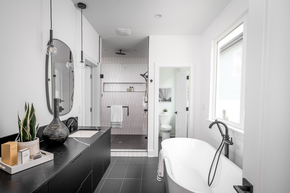 This is an example of a contemporary ensuite bathroom in Charlotte with black cabinets, a freestanding bath, an alcove shower, a one-piece toilet, white walls, porcelain flooring, a submerged sink, engineered stone worktops, black floors, a hinged door, black worktops, an enclosed toilet, double sinks, a floating vanity unit and flat-panel cabinets.