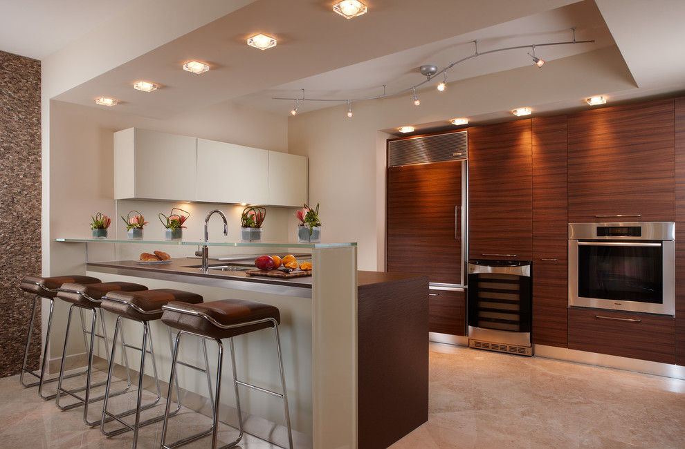 This is an example of a contemporary u-shaped kitchen in New Orleans with an undermount sink, flat-panel cabinets, medium wood cabinets, glass benchtops, panelled appliances, a peninsula, beige floor and brown benchtop.