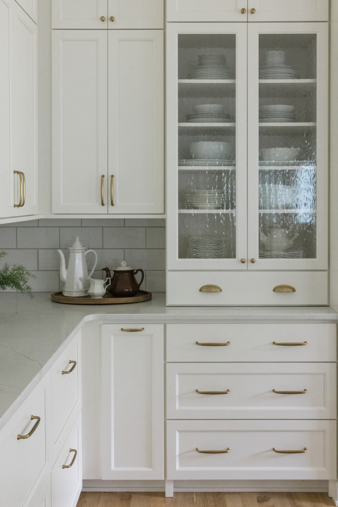 Design ideas for a classic u-shaped kitchen/diner in Other with an island, recessed-panel cabinets, white cabinets, engineered stone countertops, white splashback, metro tiled splashback, light hardwood flooring and white worktops.
