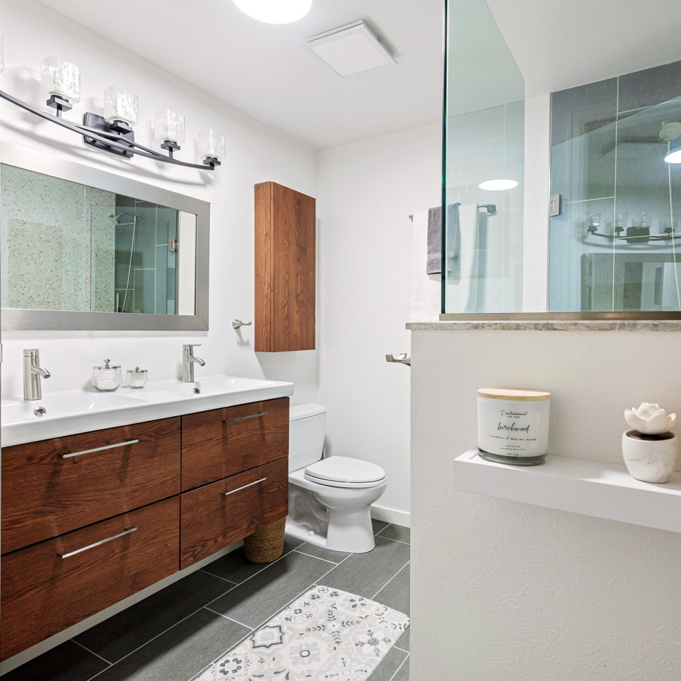 Идея дизайна: ванная комната среднего размера в стиле модернизм с плоскими фасадами, коричневыми фасадами, раздельным унитазом, серой плиткой, керамогранитной плиткой, белыми стенами, полом из керамогранита, столешницей из искусственного камня, серым полом, душем с распашными дверями, белой столешницей, сиденьем для душа, тумбой под две раковины и подвесной тумбой