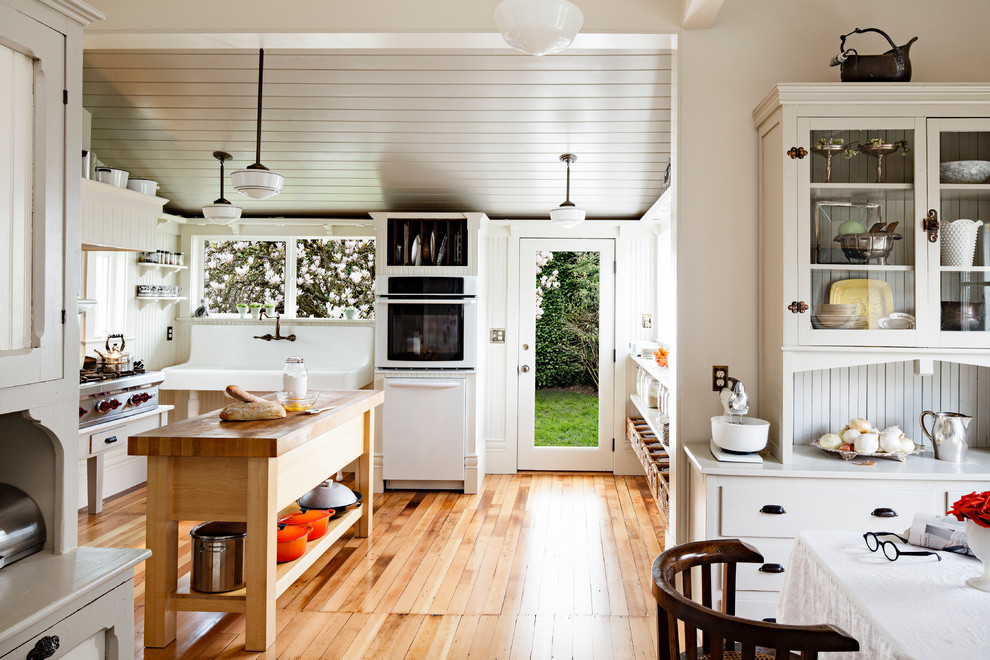 Inspiration for a mid-sized country u-shaped eat-in kitchen in Portland with wood benchtops, white splashback, white appliances, with island, beige benchtop, medium hardwood floors and brown floor.