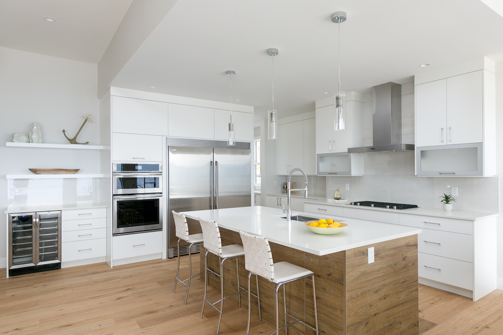 Design ideas for a contemporary l-shaped kitchen in Vancouver with an undermount sink, flat-panel cabinets, white cabinets, white splashback, stainless steel appliances, medium hardwood floors, with island and brown floor.
