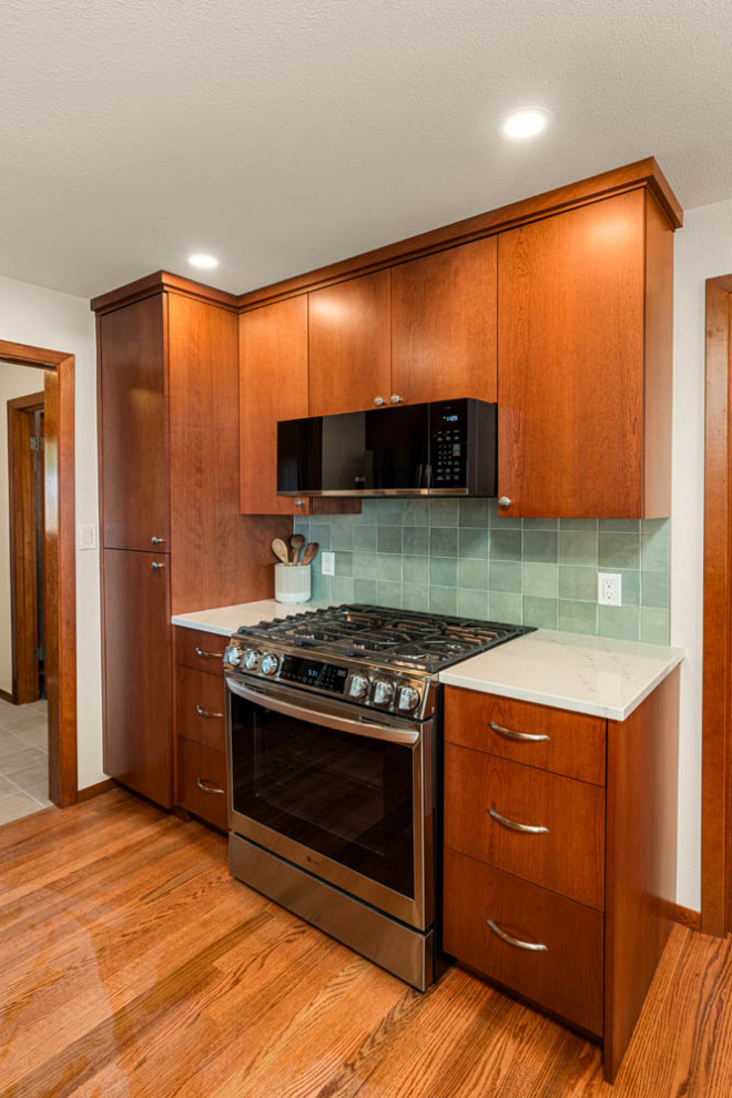 Example of a transitional l-shaped eat-in kitchen design in Seattle with flat-panel cabinets, medium tone wood cabinets, quartz countertops, green backsplash, porcelain backsplash, stainless steel appliances, a peninsula and white countertops