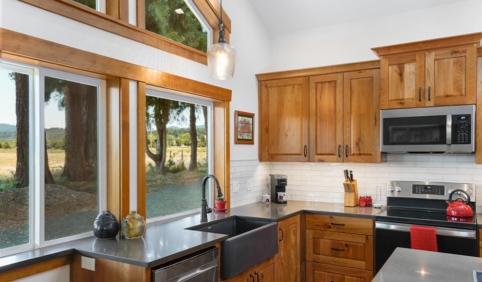 Large mountain style medium tone wood floor, brown floor and vaulted ceiling kitchen photo with a farmhouse sink, raised-panel cabinets, medium tone wood cabinets, concrete countertops, white backsplash, ceramic backsplash, stainless steel appliances, an island and gray countertops