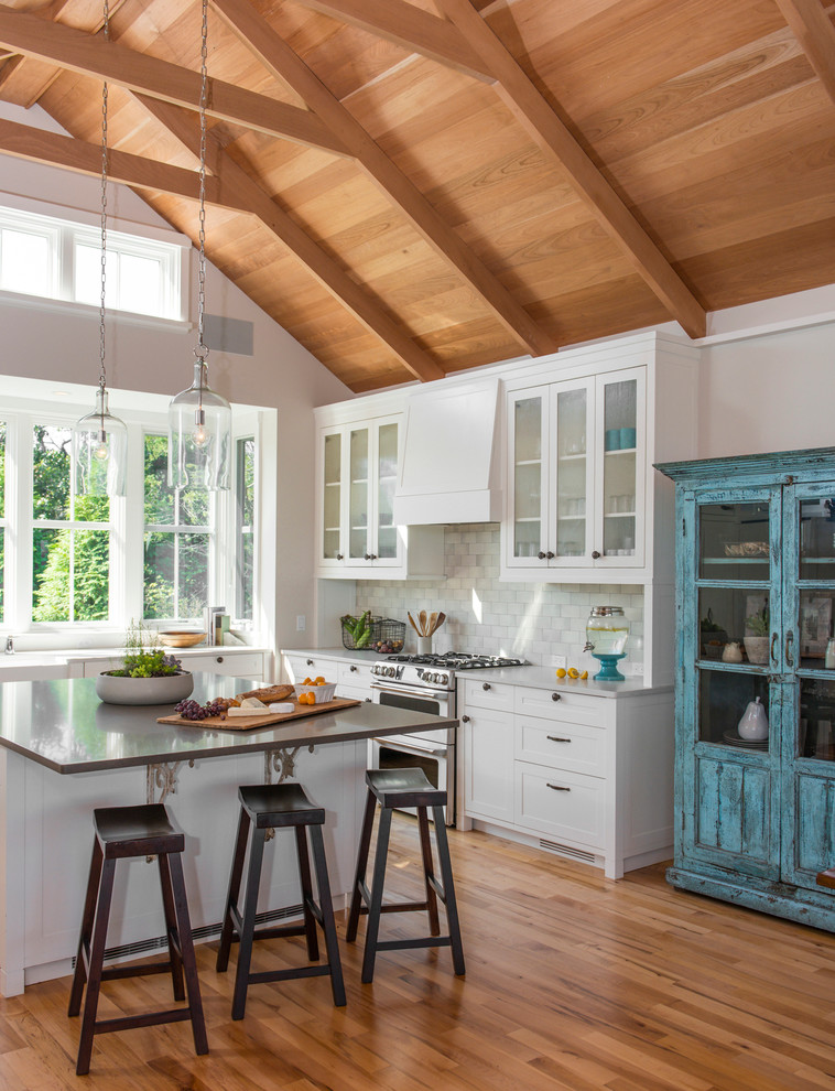 Inspiration for a mid-sized traditional u-shaped kitchen in Boston with a farmhouse sink, shaker cabinets, white cabinets, white splashback, subway tile splashback, stainless steel appliances, medium hardwood floors and with island.