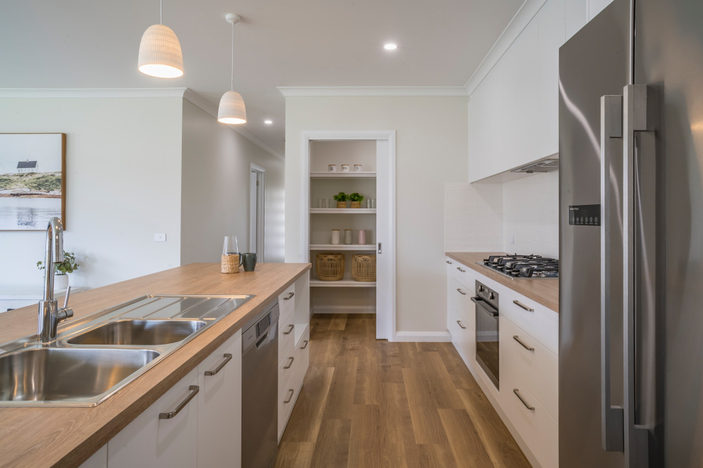 Inspiration for a mid-sized contemporary galley open plan kitchen in Other with a drop-in sink, flat-panel cabinets, white cabinets, laminate benchtops, white splashback, cement tile splashback, stainless steel appliances, vinyl floors, with island, brown floor and brown benchtop.
