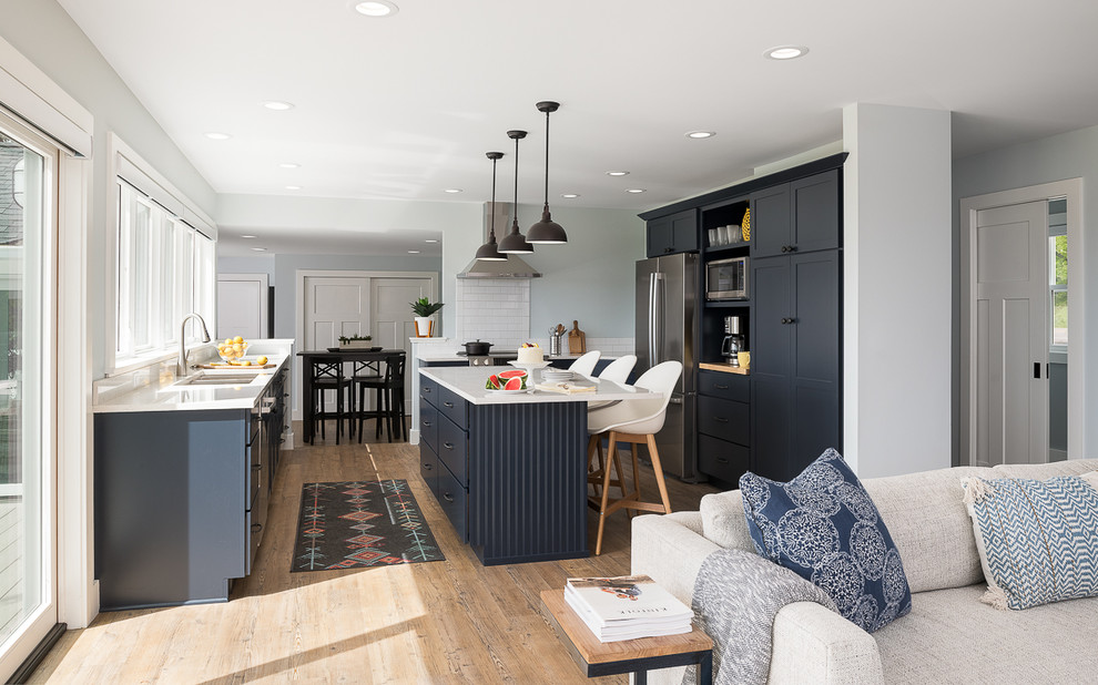 Inspiration for a mid-sized transitional l-shaped vinyl floor open concept kitchen remodel in Burlington with an undermount sink, flat-panel cabinets, blue cabinets, quartz countertops, white backsplash, porcelain backsplash, stainless steel appliances and an island