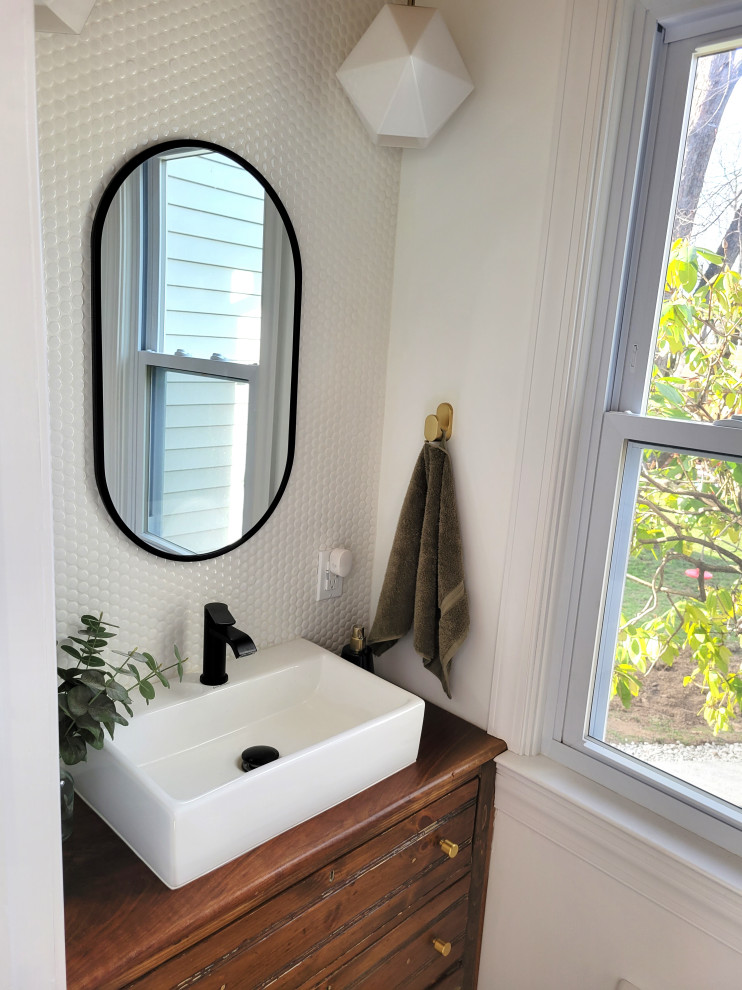 Foto på ett litet funkis toalett, med skåp i mellenmörkt trä, vit kakel, porslinskakel, svarta väggar, ett fristående handfat och träbänkskiva