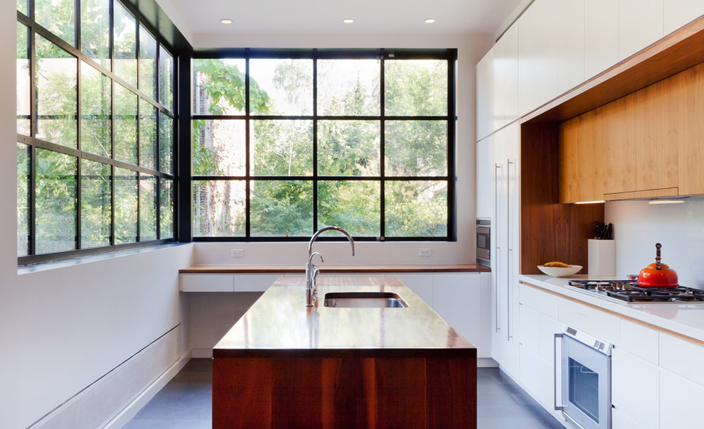This is an example of a modern kitchen in New York with flat-panel cabinets and wood benchtops.