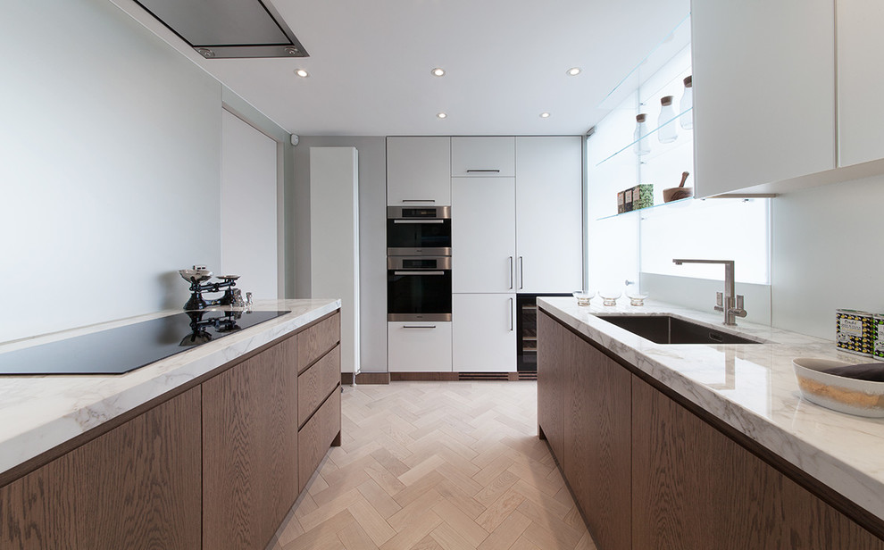 This is an example of a small midcentury u-shaped separate kitchen in London with a drop-in sink, flat-panel cabinets, dark wood cabinets, marble benchtops, stainless steel appliances, light hardwood floors and no island.