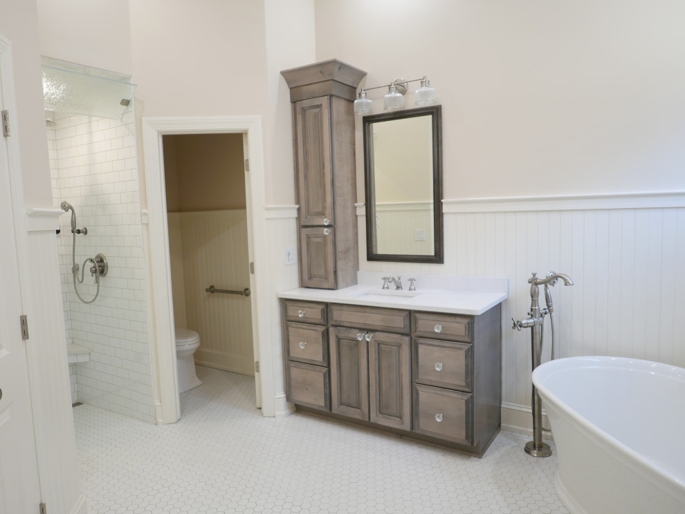 Design ideas for a large classic ensuite bathroom in Other with raised-panel cabinets, medium wood cabinets, a freestanding bath, a built-in shower, a two-piece toilet, white tiles, ceramic tiles, beige walls, porcelain flooring, a submerged sink, engineered stone worktops, white floors, a hinged door, white worktops, a wall niche, a single sink, a built in vanity unit, a vaulted ceiling and wainscoting.