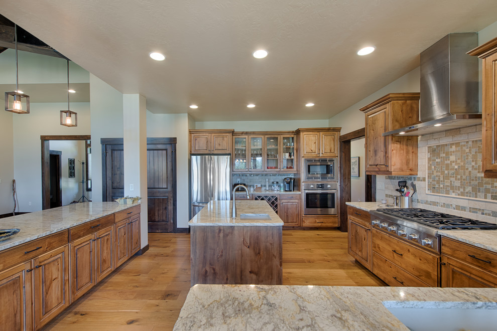 Inspiration for a country galley eat-in kitchen in Boise with a double-bowl sink, shaker cabinets, distressed cabinets, granite benchtops, beige splashback, travertine splashback, stainless steel appliances, light hardwood floors, multiple islands and brown floor.