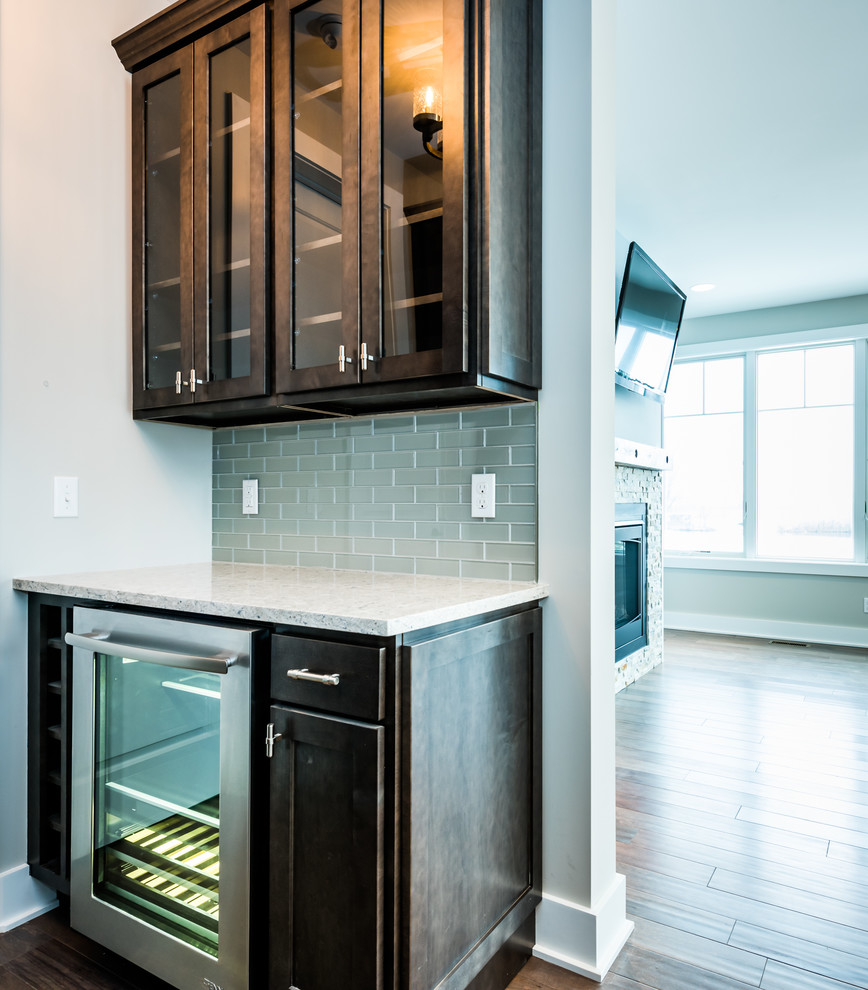 Example of a mid-sized transitional single-wall dark wood floor and brown floor home bar design in Other with no sink, glass-front cabinets, dark wood cabinets, quartz countertops, gray backsplash, gl