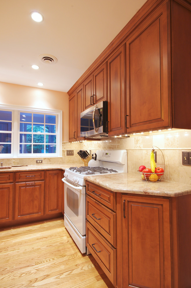 Photo of a mid-sized traditional l-shaped kitchen in Baltimore with an undermount sink, raised-panel cabinets, medium wood cabinets, granite benchtops, beige splashback, ceramic splashback, white appliances, light hardwood floors and with island.