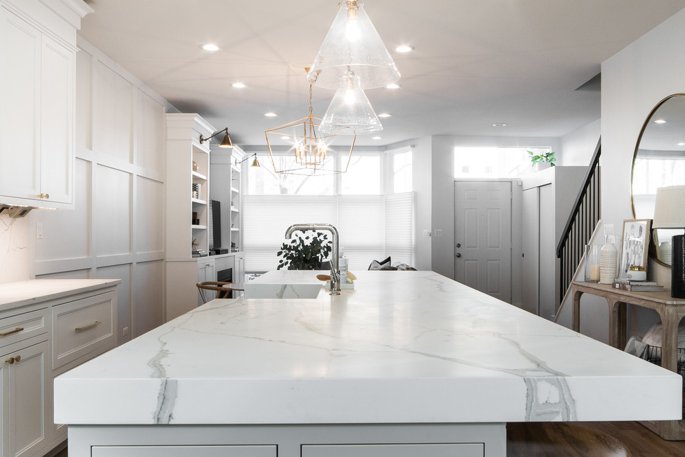 Example of a mid-sized transitional galley light wood floor and beige floor open concept kitchen design in Chicago with a farmhouse sink, recessed-panel cabinets, white cabinets, quartz countertops, stone slab backsplash, stainless steel appliances and an island