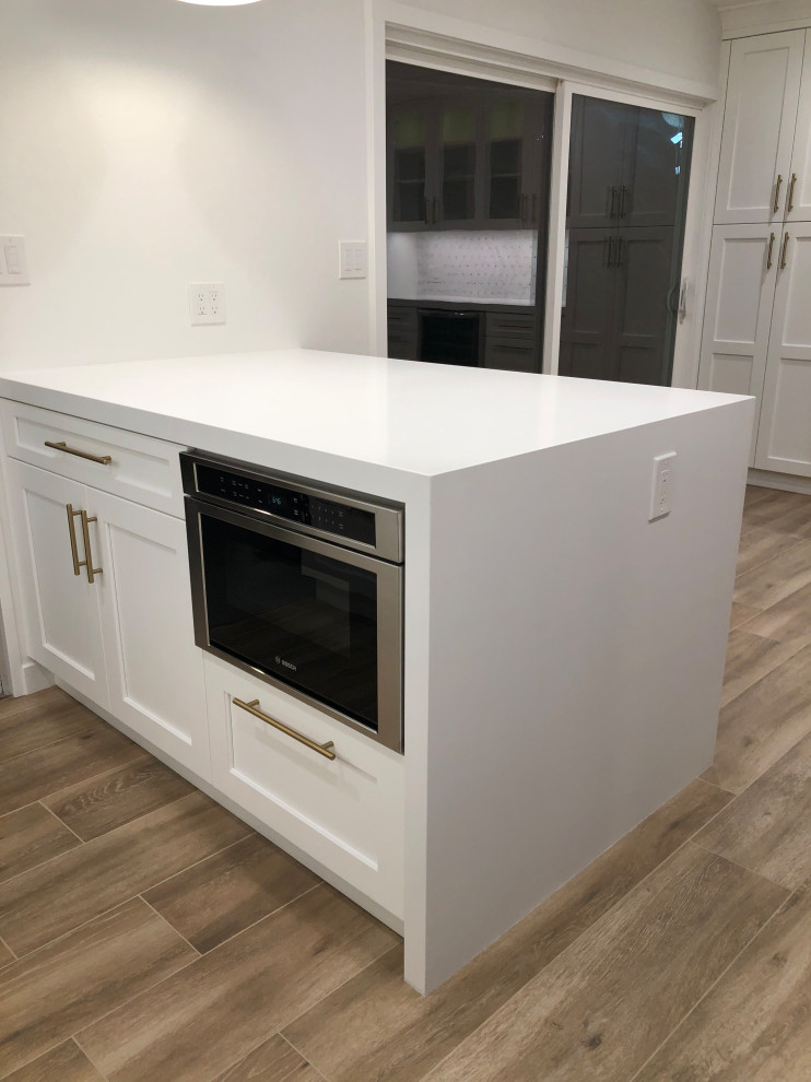 Example of a mid-sized transitional l-shaped medium tone wood floor and brown floor eat-in kitchen design in San Francisco with a farmhouse sink, recessed-panel cabinets, white cabinets, quartz countertops, white backsplash, mosaic tile backsplash, stainless steel appliances, a peninsula and white countertops